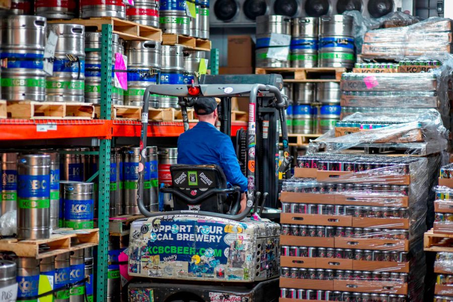 forklift driver navigating pallets of cans and racks of kegs in a brewery