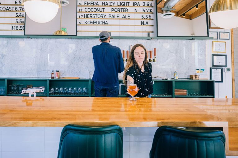 Woman serving beer over bar to empty bar seats.