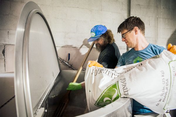 Two men adding grain to a brew kettle to brew beer