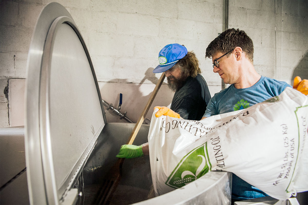 Two men adding grain to a brew kettle to brew beer
