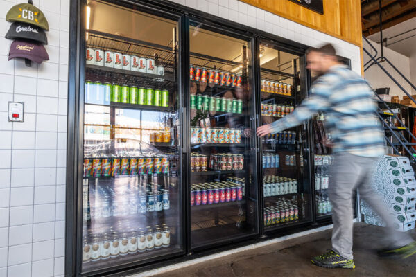 Man in plaid shirt reaches to open beer cooler in taproom