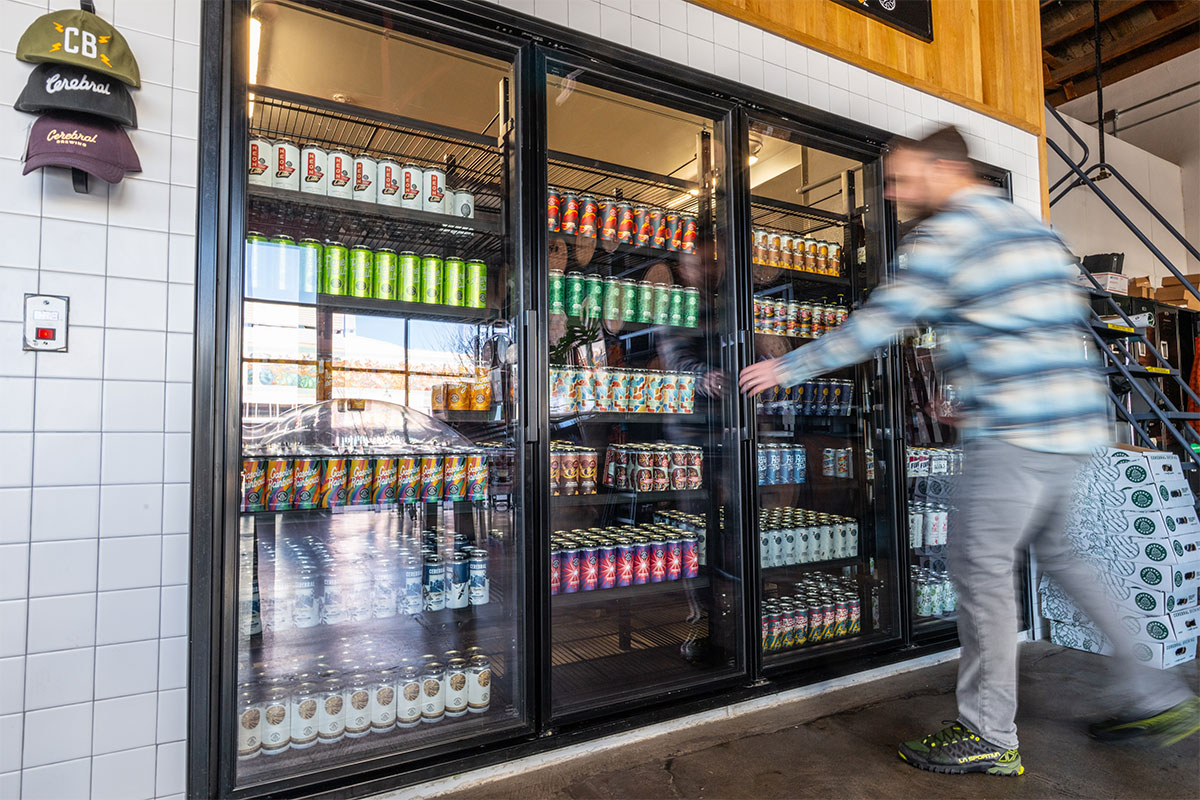 Man in plaid shirt reaches to open beer cooler in taproom