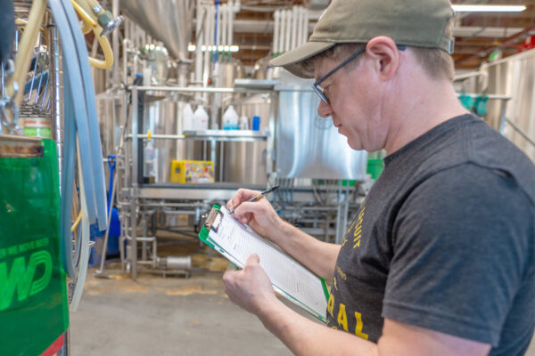 A male brewer looking at a clipboard in a brewhouse