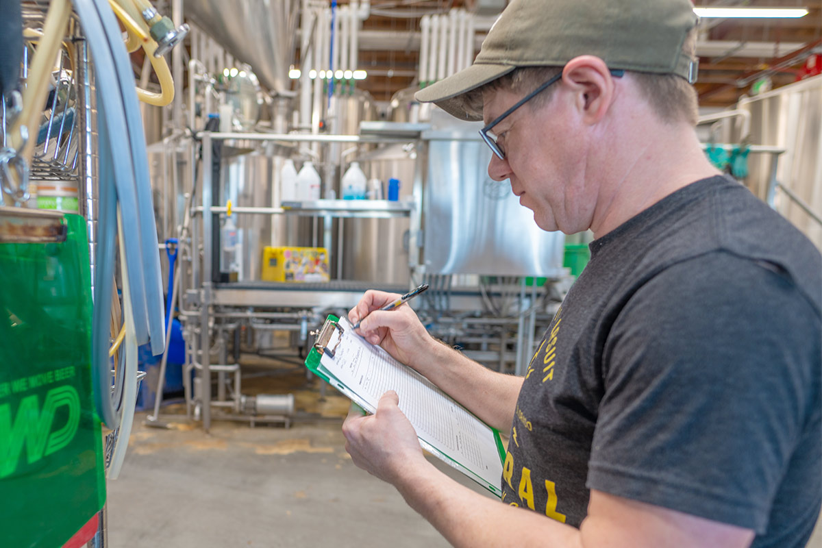 A male brewer looking at a clipboard in a brewhouse