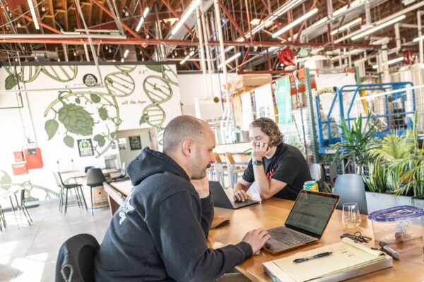 Two brewery employees looking at their laptops in a brewery taproom